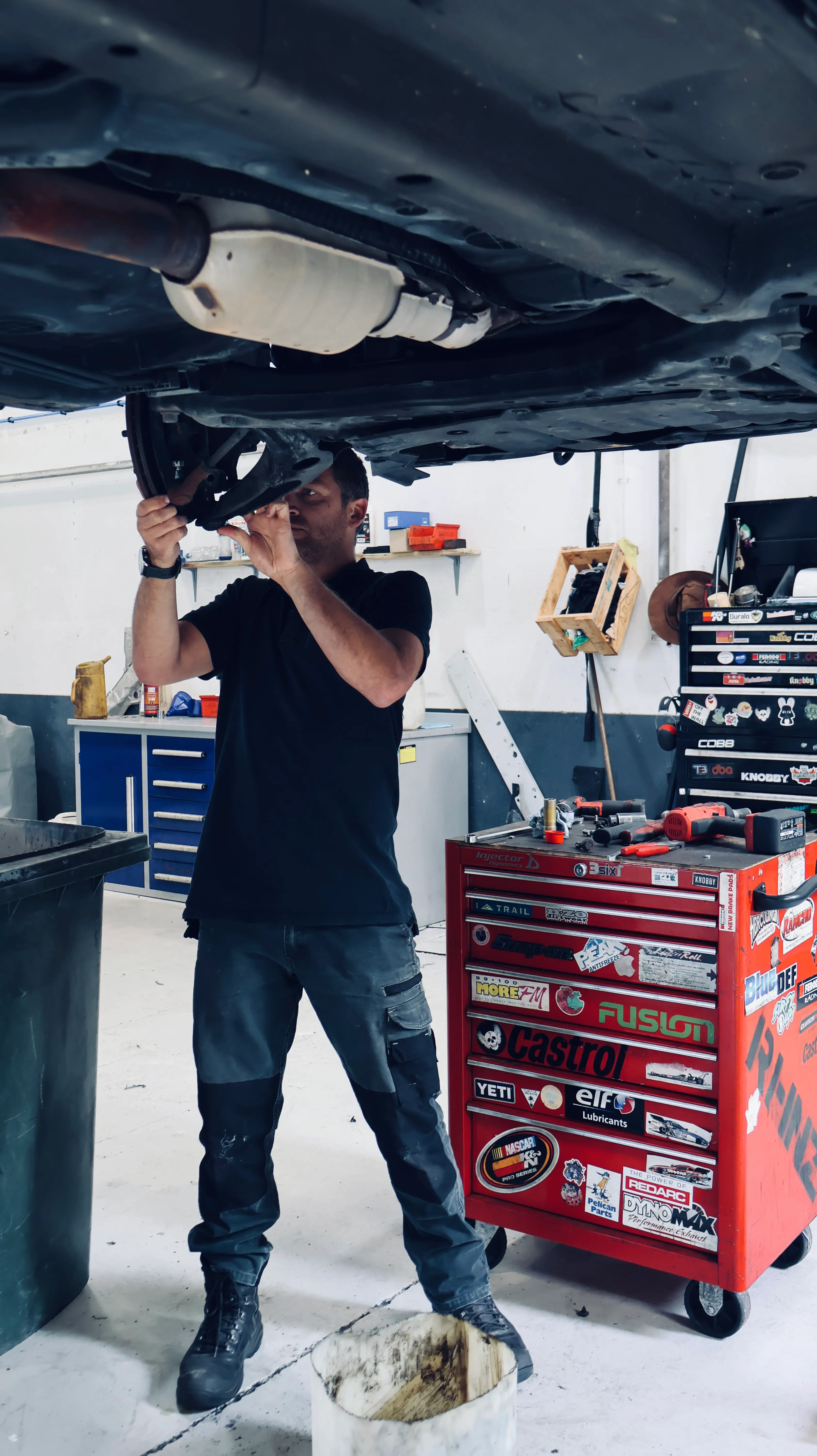 Inside the workshop with a car on the hoist and a mechanic working underneath